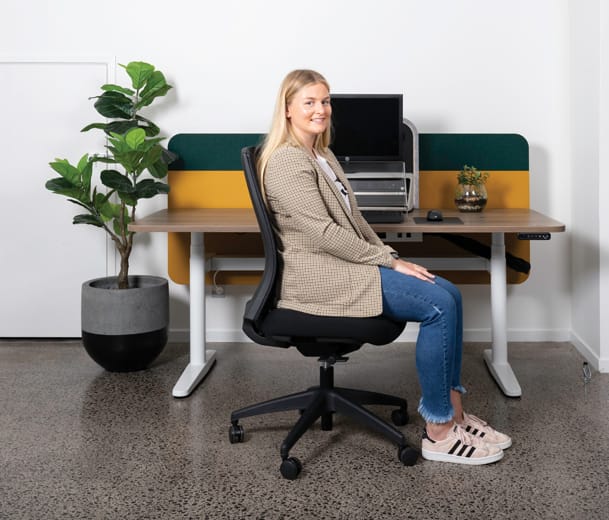 Woman seated in a Buro Mentor ergonomic office chair at a desk with yellow and green background