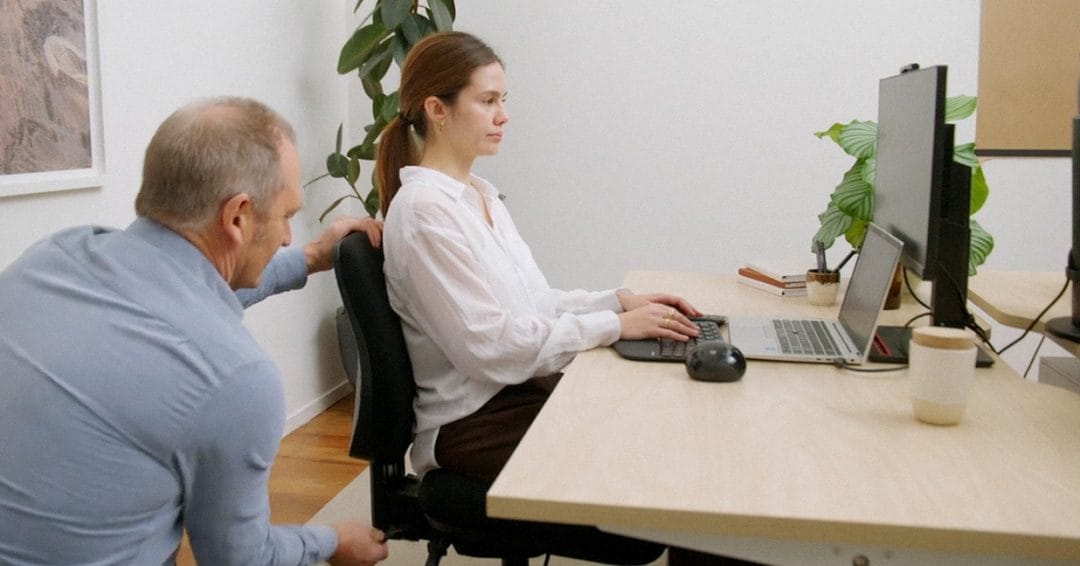 Lady sitting at desk with Ergonomist adjusting her chair
