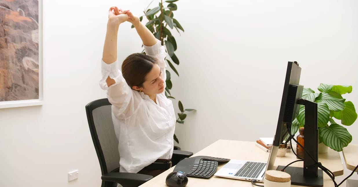 Woman in Buro chair doing arm stretches in the office