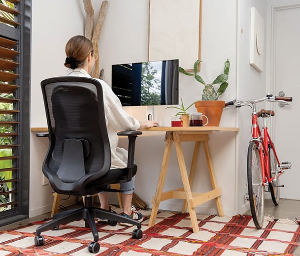 Buro Elan black ergonomic chair, back view woman working from home at wooden desk with bicycle